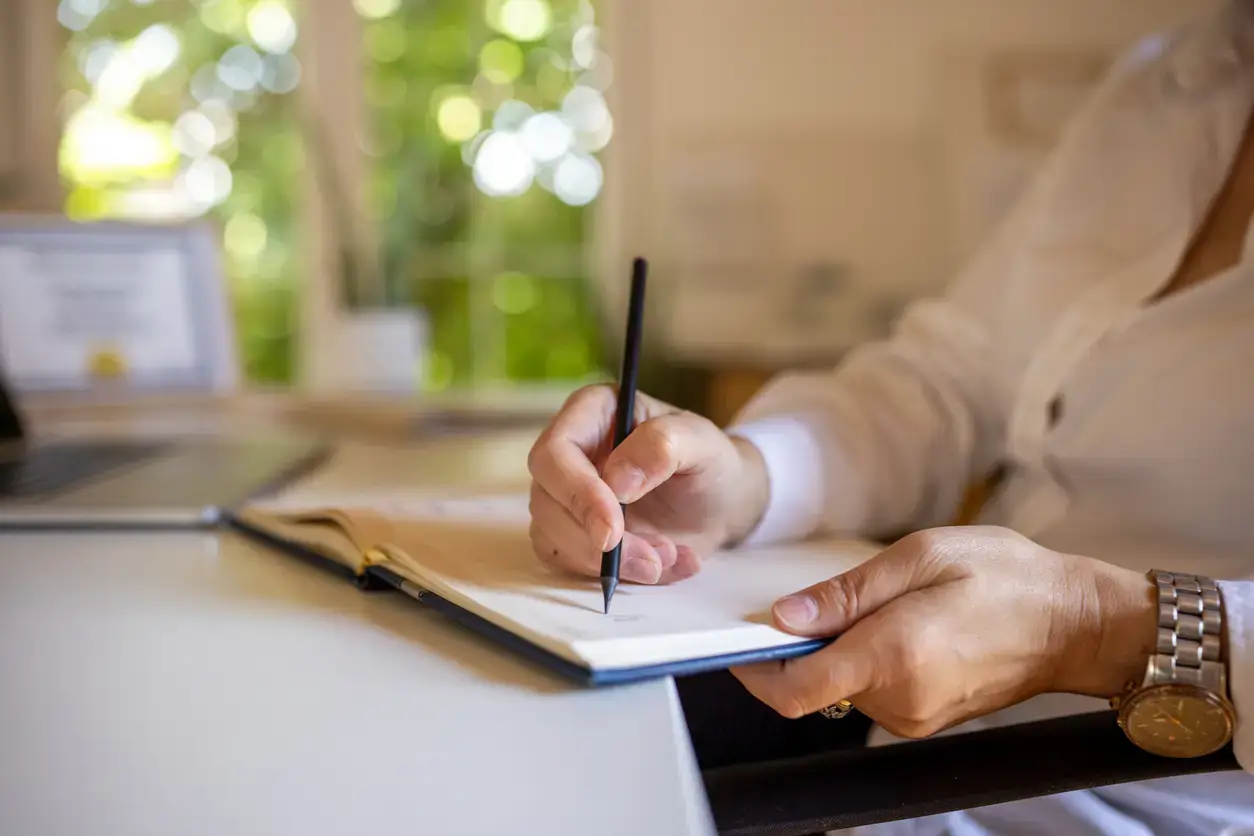 Unrecognizable mature businesswoman writing in note pad in modern office.