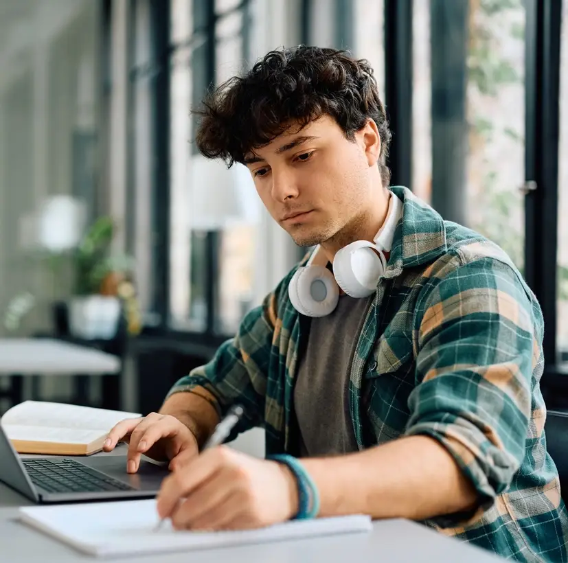 University student writing while using laptop and studying in the classroom. Copy space.
