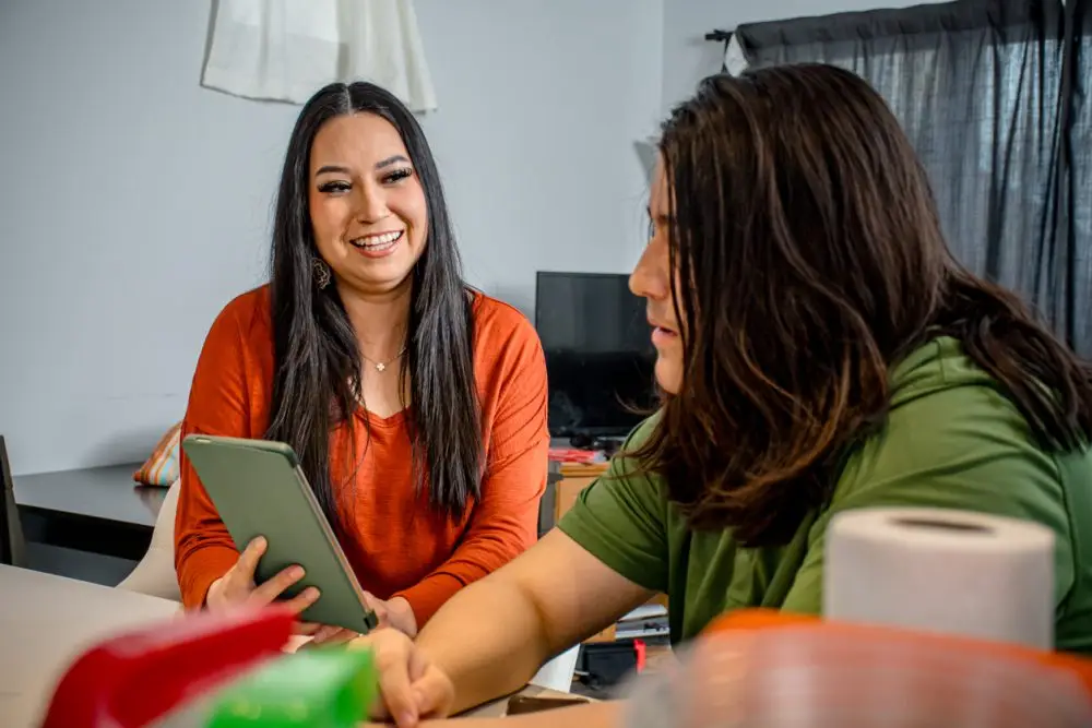 In a scene of mutual discovery, the woman captivates her teen's interest by sharing something captivating on her tablet, nurturing a bond through the joy of exploration and knowledge