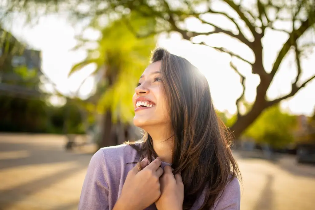Close up portrait happy young woman laughing with hands in hair in park